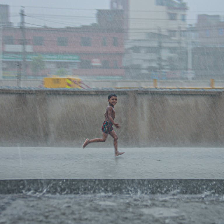 A happy child running through the rain on an urban street, expressing freedom and joy.